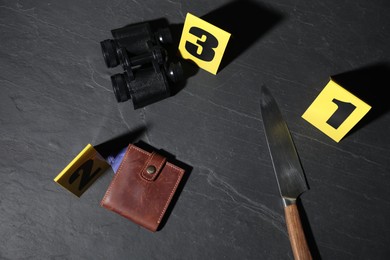 Photo of Forensic expert. Yellow evidence markers, knife, binoculars and wallet on black table, flat lay