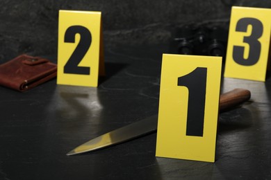 Photo of Forensic expert. Yellow evidence markers, knife and wallet on black table, closeup