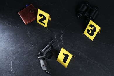 Photo of Forensic expert. Yellow evidence markers, gun and wallet on black table, above view
