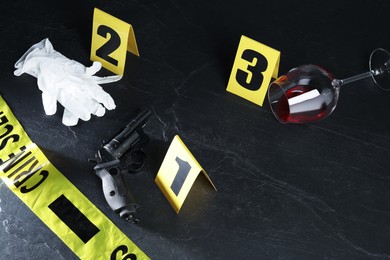 Photo of Forensic expert. Yellow crime scene tape, markers, gun, wine and gloves on black table, above view. Space for text