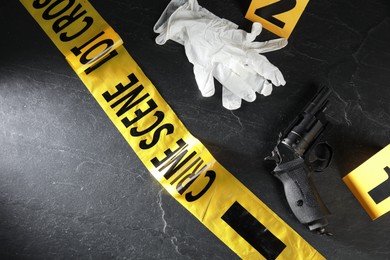 Photo of Forensic expert. Yellow crime scene tape, markers, gloves and gun on black table, above view. Space for text