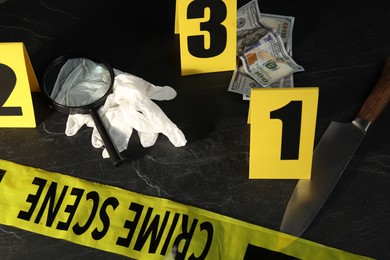 Photo of Forensic expert. Yellow crime scene tape, markers and evidences on black table, above view