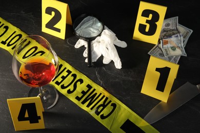 Photo of Forensic expert. Yellow crime scene tape, markers and evidences on black table, above view