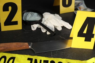 Photo of Forensic expert. Yellow crime scene tape, markers and evidences on black table, closeup