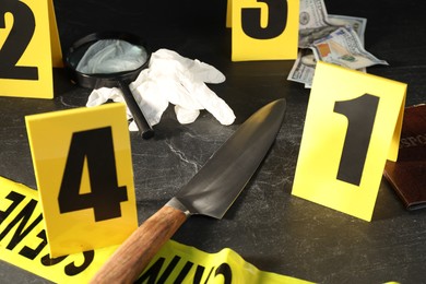 Photo of Forensic expert. Yellow crime scene tape, markers and evidences on black table, closeup