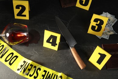 Photo of Forensic expert. Yellow crime scene tape, markers and evidences on black table, above view