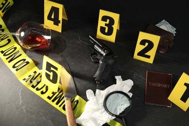Photo of Forensic expert. Yellow crime scene tape, markers and evidences on black table, above view