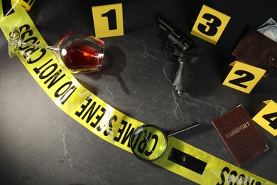 Photo of Forensic expert. Yellow crime scene tape, markers and evidences on black table, above view