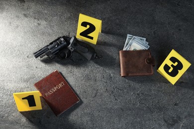 Photo of Forensic expert. Yellow evidence markers, wallet with money, gun and passport on grey table, above view