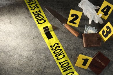 Photo of Forensic expert. Yellow crime scene tape, evidence markers, wallet with money, knife and passport on grey table, above view. Space for text