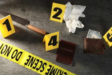Photo of Forensic expert. Yellow crime scene tape, markers and evidences on grey table, above view