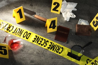 Photo of Forensic expert. Yellow crime scene tape, markers and evidences on grey table, above view