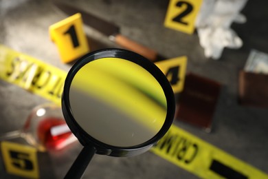 Photo of Forensic expert. Looking at yellow crime scene tape, markers and evidences through magnifying glass on grey table, selective focus