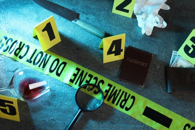 Photo of Forensic expert. Yellow crime scene tape, markers and evidences on grey table, above view