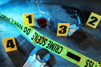 Photo of Forensic expert. Yellow crime scene tape, markers and evidences on grey table, above view