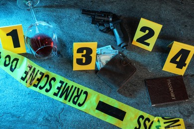 Photo of Forensic expert. Yellow crime scene tape, markers and evidences on grey table, above view