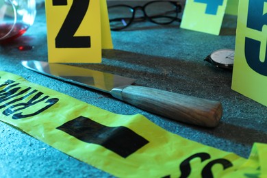 Photo of Forensic expert. Yellow crime scene tape, markers, knife and other evidences on grey table, closeup