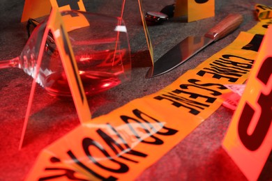 Photo of Forensic expert. Yellow crime scene tape, markers, knife and glass of wine on grey table, closeup