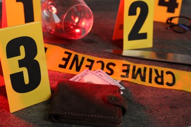 Photo of Forensic expert. Yellow crime scene tape, markers, wallet with money, glass and glasses on grey table, closeup