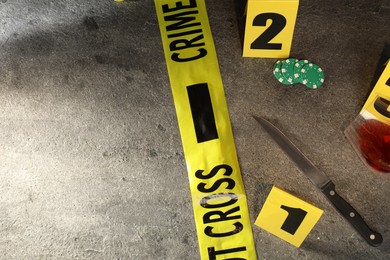 Photo of Forensic expert. Yellow crime scene tape, markers, knife and glass of wine on grey table, flat lay. Space for text
