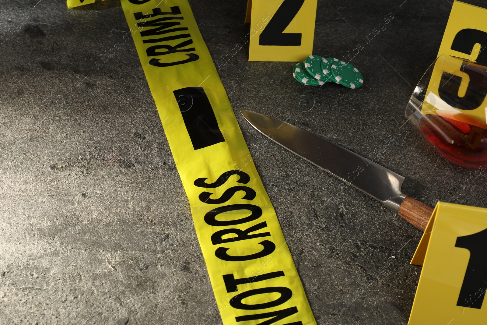 Forensic expert. Yellow crime scene tape, markers, knife and glass of wine on grey table, closeup. Space for text Photo of Forensic expert. Yellow crime scene tape, markers, knife and glass of wine on grey table, closeup. Space for text