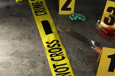 Photo of Forensic expert. Yellow crime scene tape, markers, knife and glass of wine on grey table, closeup. Space for text