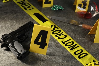 Photo of Forensic expert. Yellow crime scene tape, markers and evidences on grey table, closeup