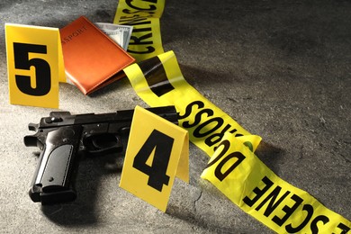 Photo of Forensic expert. Yellow crime scene tape, gun, passport and money on grey table, closeup. Space for text