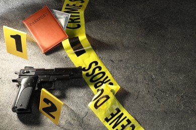 Photo of Forensic expert. Yellow crime scene tape, gun, passport and money on grey table, flat lay. Space for text