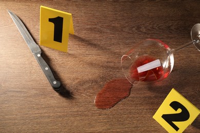 Photo of Forensic expert. Knife, glass with wine and yellow evidence markers on wooden table, above view