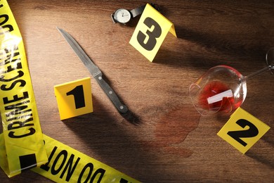 Photo of Forensic expert. Yellow crime scene tape, knife, glass with wine, watch and evidence markers on wooden table, flat lay