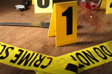Photo of Forensic expert. Yellow crime scene tape, markers and evidences on wooden table, closeup