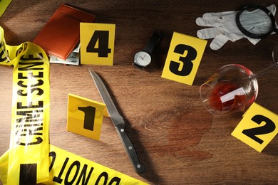 Photo of Forensic expert. Yellow crime scene tape, markers and evidences on wooden table, above view