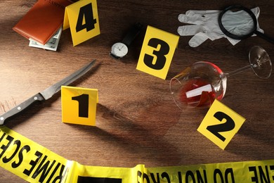 Photo of Forensic expert. Yellow crime scene tape, markers and evidences on wooden table, above view