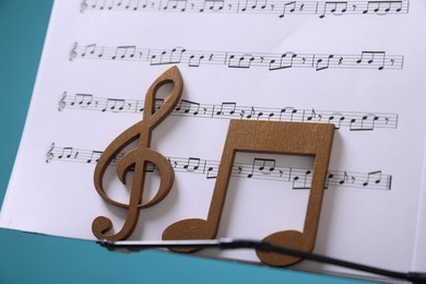Photo of Stand with music sheets and wooden notes on light blue background, closeup