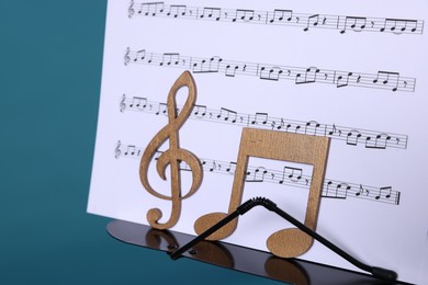 Photo of Stand with music sheets and wooden notes on light blue background, closeup