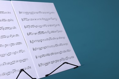 Photo of Note stand with music sheets on light blue background, closeup. Space for text