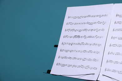 Photo of Note stand with music sheets on light blue background, closeup. Space for text