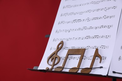 Photo of Stand with music sheets and wooden notes on red background, closeup. Space for text