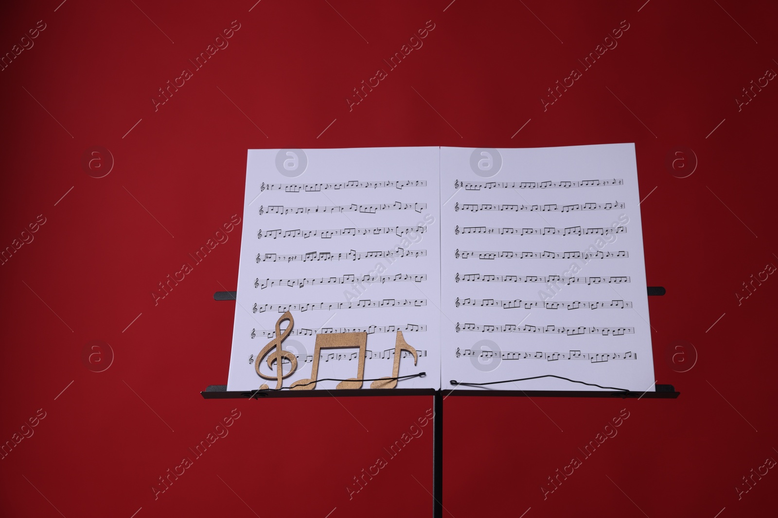 Stand with music sheets and wooden notes on red background Photo of Stand with music sheets and wooden notes on red background