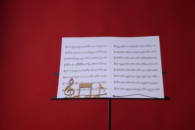 Photo of Stand with music sheets and wooden notes on red background