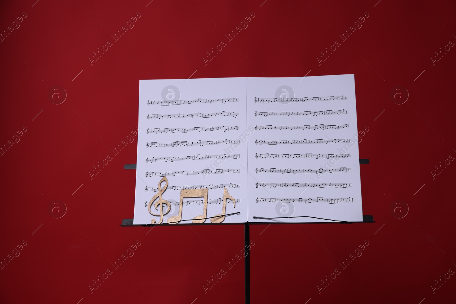 Stand with music sheets and wooden notes on red background Photo of Stand with music sheets and wooden notes on red background