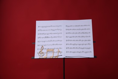 Photo of Stand with music sheets and wooden notes on red background