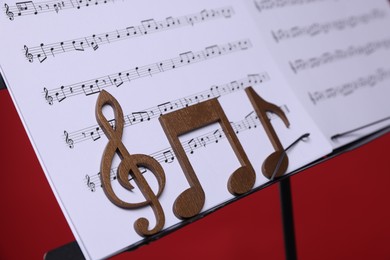 Photo of Stand with music sheets and wooden notes on red background, closeup