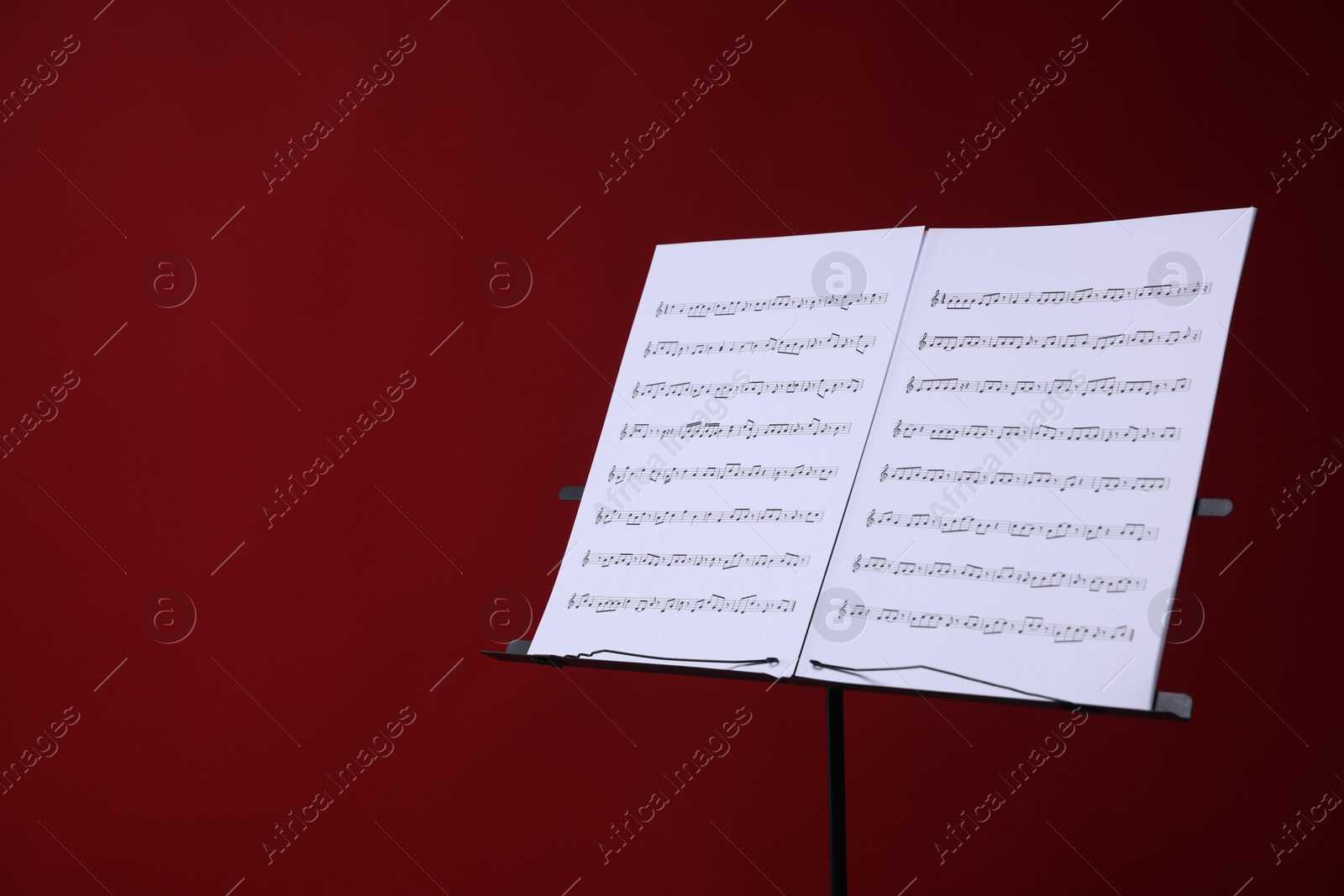Note stand with music sheets on red background, space for text Photo of Note stand with music sheets on red background, space for text