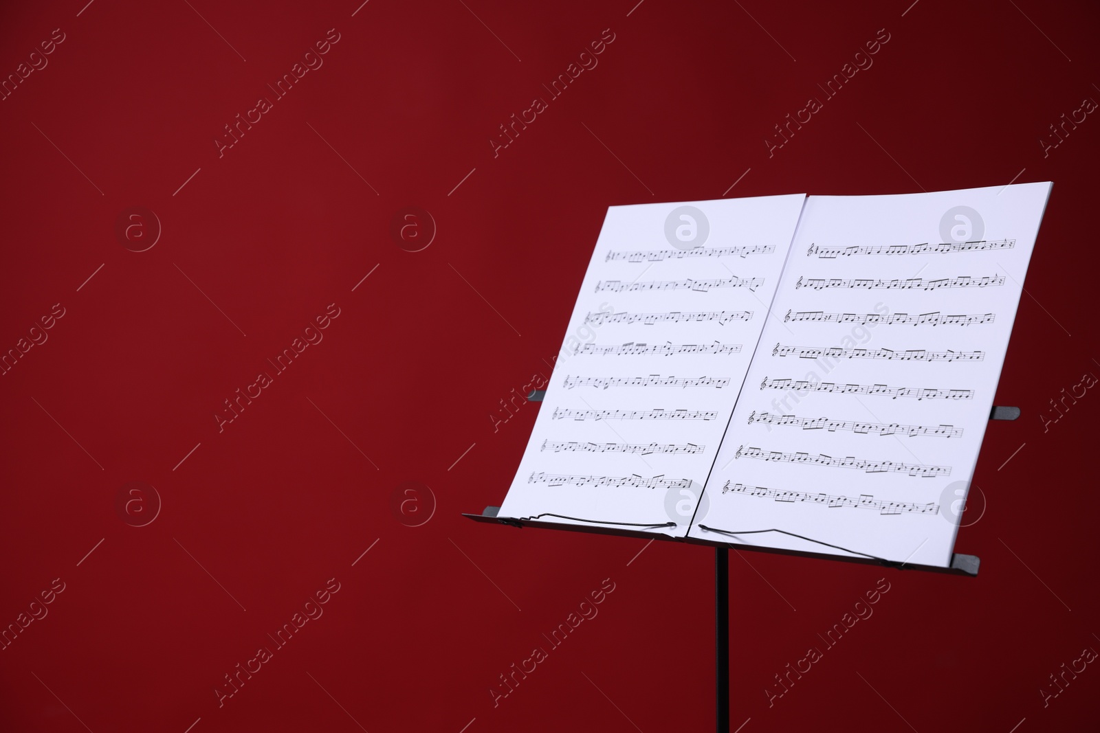 Note stand with music sheets on red background, space for text Photo of Note stand with music sheets on red background, space for text