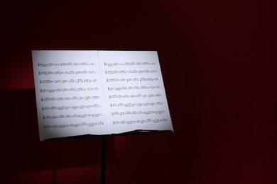 Photo of Note stand with music sheets on dark red background, space for text