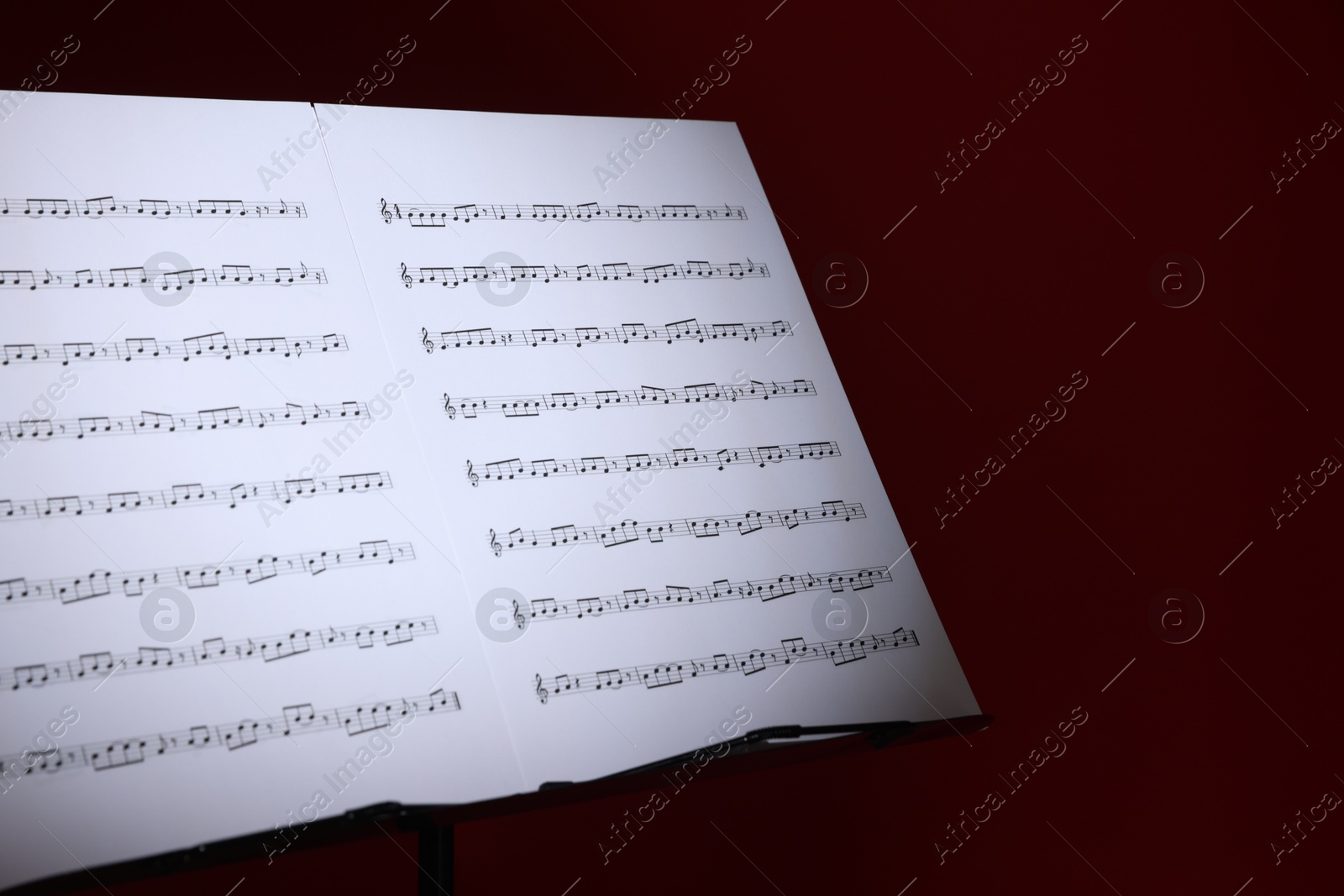 Note stand with music sheets on dark red background, closeup. Space for text Photo of Note stand with music sheets on dark red background, closeup. Space for text