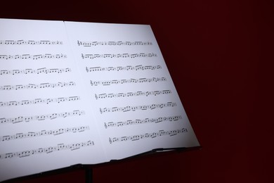 Photo of Note stand with music sheets on dark red background, closeup. Space for text