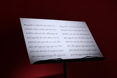 Photo of Note stand with music sheets on dark red background, closeup
